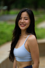 Portrait of a beautiful young Asian sportswoman smiling in a park, wearing sportswear