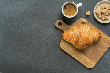 Fresh croissant and coffee on wooden board with sugar cubes on black background