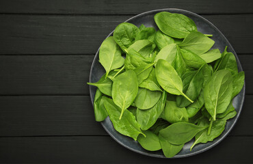 Fresh spinach leaves on dark plate on black wooden background