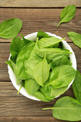 Baby spinach leaves with water drops in white bowl on grey wooden background. Vertical photo