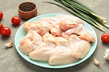 Raw chicken wings with ingredients for cooking on dark plate on grey concrete background