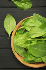 Spinach leaves in a wooden plate on black background. Vertical photo