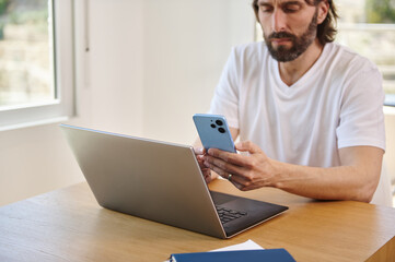 Young Man Working Remotely from Home Using Laptop and Smartphone