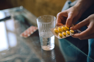 A tired young woman is sitting on the couch and taking medicine with water