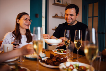 A young woman and a man are drinking champagne and eating in the living room. A happy couple family dinner. A husband and wife are having lunch and laughing at a set table.