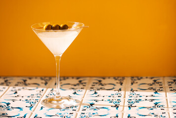 An elegant margarita cocktail glass with with green olives on a yellow background. A delicious...