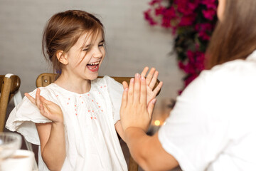 A little girl in a fancy dress is playing with her older sister. The cute child laughs and claps his hands. The kid is having fun with her mom.
