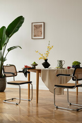 Modern dining space with green foliage in a glass vase, lime arrangement, and soft natural light. A...