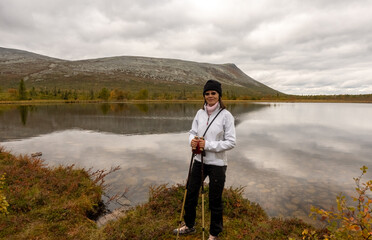 Fototapeta premium Woman hiking in Swedish Lapland during autumn, standing by a tranquil mountain lake with Nordic hills in the background. Scenic wilderness adventure in Scandinavia with vibrant fall colors