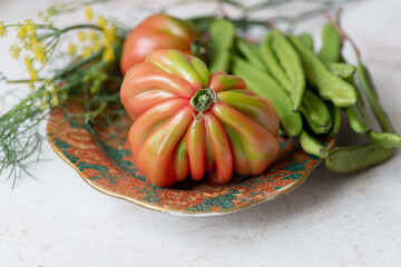 Heirloom tomato, fresh green carob beans and fennel with soft feathery leaves and stems on a decorative plate. Ideal for recipe blogs, farm-to-table branding, or packaging design.