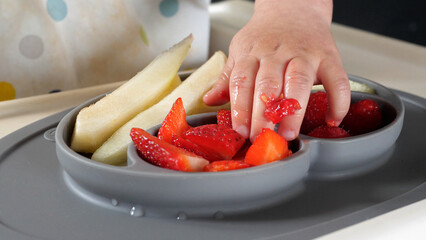 Baby taking a piece of strawberry with his dirty small hand, baby led weaning method