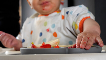 Baby taking fruit pieces from a grey silicone plate, baby led weaning