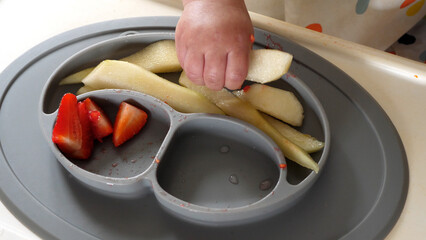 Baby taking a piece of pear with his dirty small hand, baby led weaning method