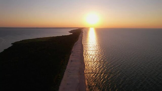 Sunset over the Hel Peninsula with sun reflection on calm sea &ndash; aerial view.
Zach&oacute;d słońca nad P&oacute;łwyspem Helskim z odbiciem słońca na spokojnym morzu &ndash; widok z drona.

