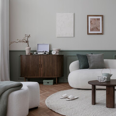 Warm and cozy living room interior with mock up poster frame, boucle sofa, wooden sideboard, coffee table, stylish lamp, gramophone, vase with leaves and personal accessories. Home decor. Template.