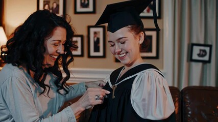 Proud mother carefully adjusting graduation gown and pinning tassel, sharing heartwarming moment of love and support with smiling daughter before academic milestone
