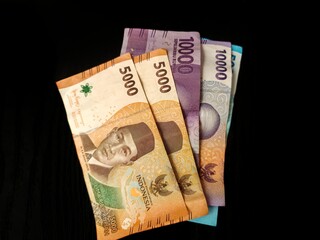 Close-up of Indonesian Rupiah banknotes in various denominations (5000, 10000, 50000) spread on black background