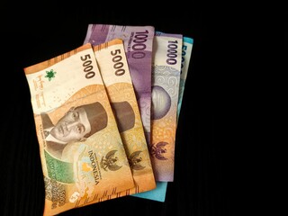 Close-up of Indonesian Rupiah banknotes in various denominations (5000, 10000, 50000) spread on black background