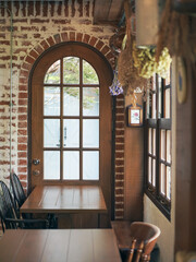 Vintage wooden door. A vintage corner with wooden table and chairs by the window and door. Soft window light. Vintage film grained filter applied. Selective focus on the glass wooden door.