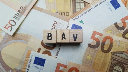 BAV acronym made of wooden letter cubes on pile of Euro banknotes. Betriebliche Altersvorsorge...