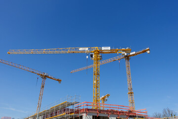 Construction site with multiple tower cranes working on new residential buildings under a clear blue sky. Concept of urban development, affordable housing, economy, and infrastructure growth