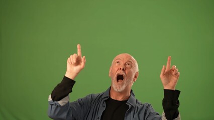 A mature man is joyfully gesturing with both hands raised while looking upward against a solid green background, conveying strong emotions and energy.
