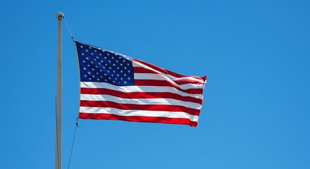 Obraz premium American Flag Waving Proudly Against a Clear Blue Sky on Flagpole, Symbol of Patriotism and National Pride on Sunny Day.