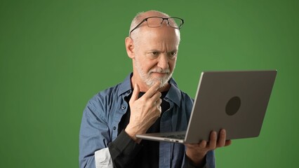 Mature man with gray hair and glasses examines his laptop with a pensive expression, set against a solid green screen background for product announcements.