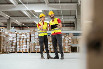 Man and woman in helmets and safety vests reviewing logistics data on tablet, discussing workflow.