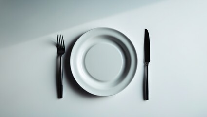 A white ceramic dish accompanied by a fork and knife, set against a plain background