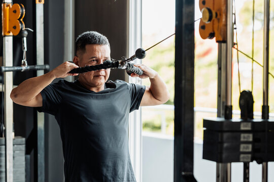 Southeast Asian man in his 50s performing face pulls with a rope attachment at an open-air gym to target rear delts.