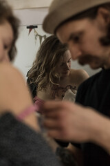 Tattoo artist creating a custom design for a young woman in a cozy Tbilisi studio. Details of the process, tattoo tools, ring light photography, and creative atmosphere