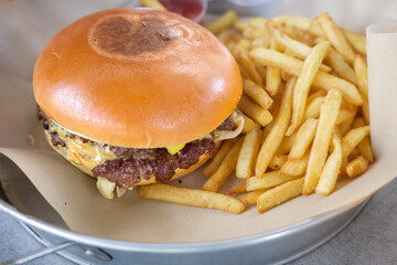 Delicious classic cheeseburger with a juicy beef patty and melted cheese, served with a generous portion of crispy golden french fries on a metal tray. A perfect fast food meal for lunch or dinner.