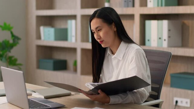 Confident Asian Japanese businesswoman female girl Korean Chinese business woman office worker secretary manager lawyer talk online call laptop remote meeting client analyzing documents folder indoor