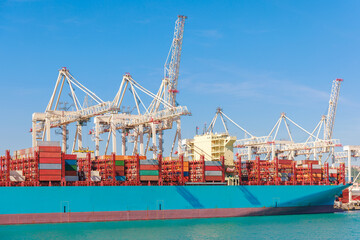 Large cargo ship is docked at a bustling shipping port, where cranes are actively loading...