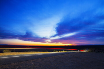 Light trails of a car driving down the road at sunset