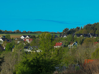 On the horizon, a small village, houses, a forest, and a blue sky are visible.