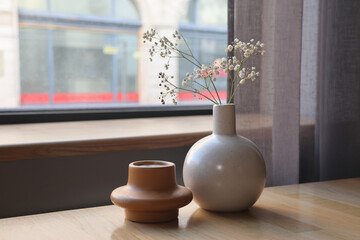 Minimalist ceramic vases on wooden table by window.