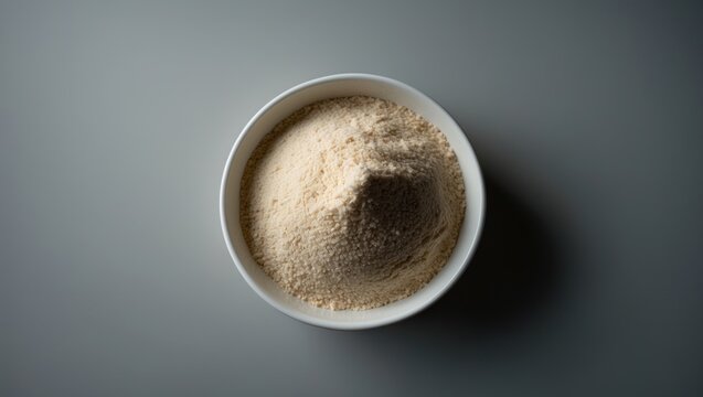 Gray background with a white ceramic bowl of Organic Ragi or Finger Millet Flour seen from above