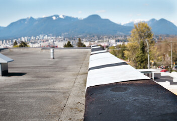 Self-adhered waterproof membrane on flat roof. Temporary or permanent peel-and-stick waterproof membrane repair. 2-ply SBS or modified bitumen roofing system. Roof coping removed. Selective focus.