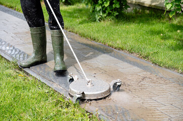 Professional paving stone cleaning. Person using a surface cleaner on a paved outdoor walkway during a sunny day in a residential area