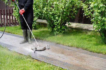 Power washing concrete walkways in a residential garden during a sunny afternoon for thorough cleaning and maintenance. Professional paving stone cleaning.