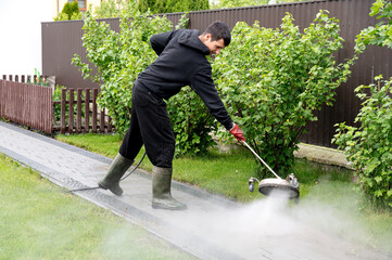 Man cleaning a walkway with a pressure washer in a residential garden on a sunny day. Professional...