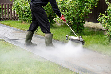 Pressure washing patio using high-pressure equipment in a residential garden setting on a cloudy day. Professional paving stone cleaning.