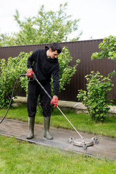Man using high-pressure cleaner to wash a patio in a garden on a sunny day. Professional paving stone cleaning.