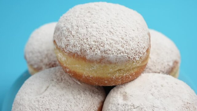 A stack of donuts in powdered sugar are rotating on a blue background. The donuts are covered with powdered sugar. The donuts are stacked on top of each other.