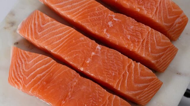 A piece of salmon is cut into four pieces. The pieces are on a marble counter. The salmon is cut in half lengthwise
