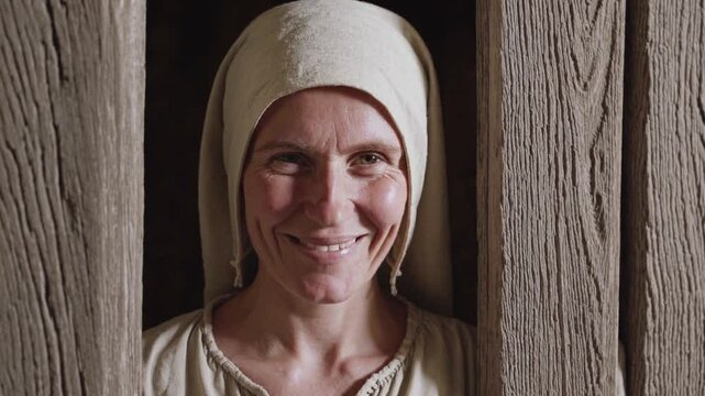 Femme m&eacute;di&eacute;vale souriante en coiffe, debout dans un cadre en bois rustique

