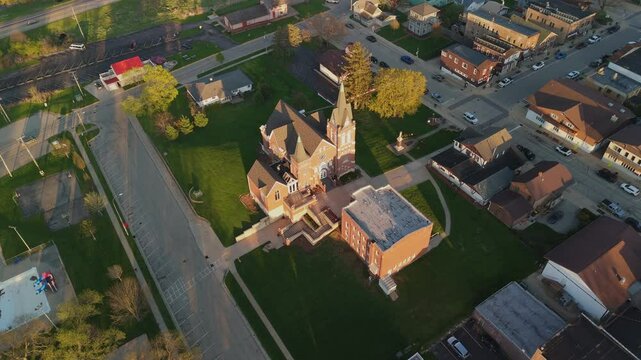 Drone video flying over New Glarus Wisconsin at sunset showing city buildings, rooftops, and the Swiss United Church of Christ in golden light.