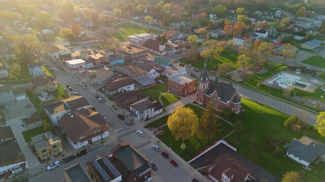 Drone video flying over New Glarus Wisconsin at sunset showing city buildings, rooftops, and the Swiss United Church of Christ in golden light.